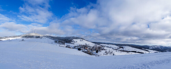Panoramablick auf den Schwarzwald im Winter. Verschneite Berglandschaften und bewaldete H&uuml;gel mit Blick auf das Dorf Gersbach, gegen&uuml;ber dem Gipfel des Rohrenkopfes und seinem Windpark
