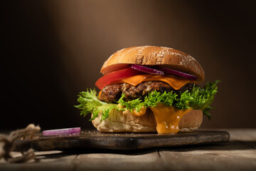 Homemade hamburger on a wooden cutting board against a dark wall