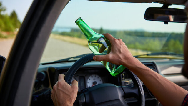Drunk driving danger with alcohol bottle in hand, reckless behavior behind the wheel, impaired driver operating a vehicle, road safety violation and lawbreaking during daylight on a country road