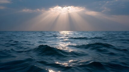 Golden sunbeams break through clouds over a calm blue ocean at sunset