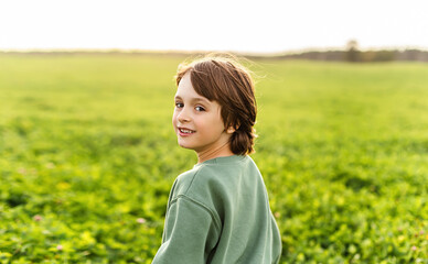 Smiling boy in green field, happy childhood, nature lifestyle, summer, freedom, copy space.