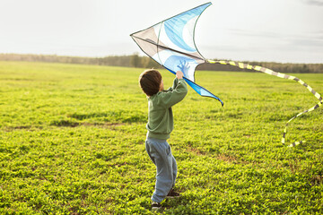 Child flying a kite outdoors in green field, happy childhood, freedom, play, nature, copy space.