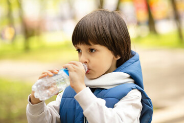 Child drinking water outdoors from bottle, healthy hydration, active lifestyle, natural light, copy space.