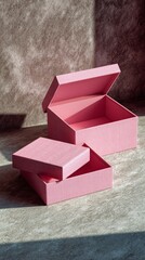 Two stylish pink storage boxes with opened lids are arranged on a textured background, beautifully illuminated by natural sunlight, highlighting their elegant design.