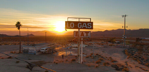 DRONE: Flying around abandoned gas station and diner in Mojave desert at sunset.