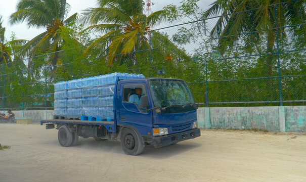 Old lorry delivers pallets full of bottled water to the harbor of exotic island.