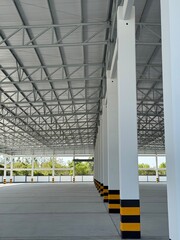 Interior view of a large empty warehouse with white columns, steel roof truss structure, concrete floor, and natural daylight, suitable for logistics, factory, or storage use.