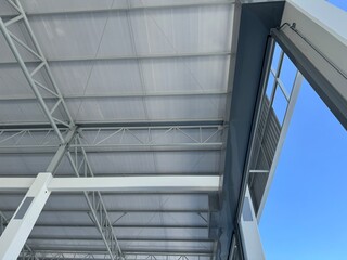 Interior view of a modern warehouse roof featuring steel trusses, insulated metal panels, and structural beams, captured from a low angle with blue sky visible.