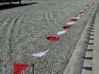 Red and white safety flags tied along a rope marking a boundary on a gravel surface beside a concrete curb, commonly used for construction site safety and hazard warning.