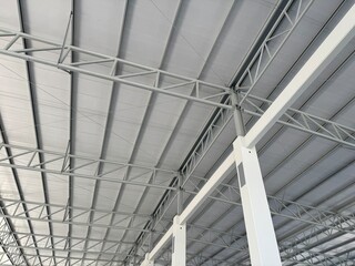 Interior view of an industrial warehouse roof featuring steel trusses, metal beams, and insulated roof panels, showing modern construction, strength, and clean structural design.