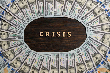 Wooden letters with the inscription crisis in the center around $100 American paper bills. Business, finances, cash and money saving concept in USA