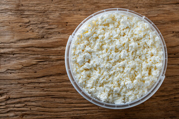 White cottage cheese or fresh milk curd in a plastic container, closeup, top view, copy space. Homemade cottage cheese texture