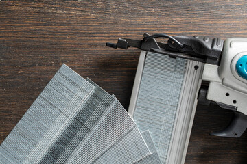 The part hammer of a power nail gun with of strips of finishing nails on wooden background. Pneumatic nail gun with metal brads, closeup, top view