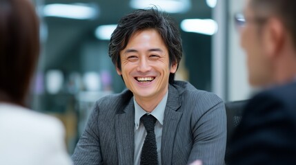 In a modern boardroom, a man in a suit discusses strategies with two colleagues. The man highlights key points while the colleagues engage in focused conversation about business.