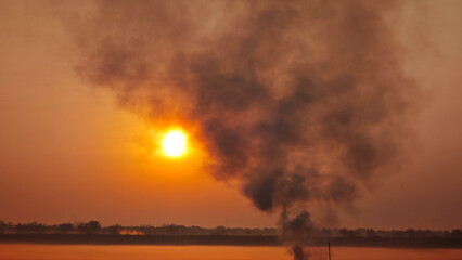 Obraz premium Fires caused by burning agricultural waste such as dry grass and rice straw produce thick smoke, which is a cause of air pollution during sunrise.