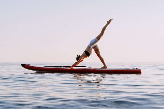 Woman practicing SUP yoga in sea at sunset.