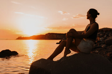 Woman wearing in yoga clothes relaxing at seaside at sunset or sunrise.