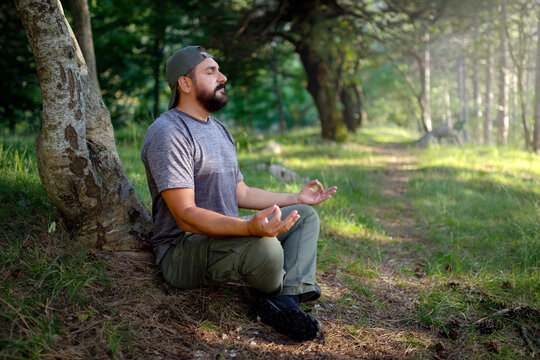 A man meditating in a forest. The practice, sometimes referred to as "forest bathing" or forest meditation, involves connecting with nature to find calm, reduce stress, and improve awareness. - Powered by Adobe