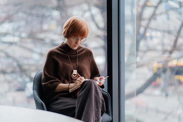 Middle aged consultant writing plans in notebook near office window