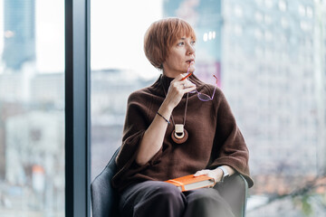 Thoughtful businesswoman holding planner by window