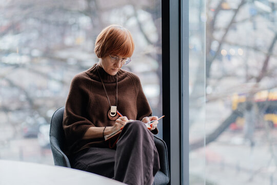 Middle aged consultant writing plans in notebook near office window