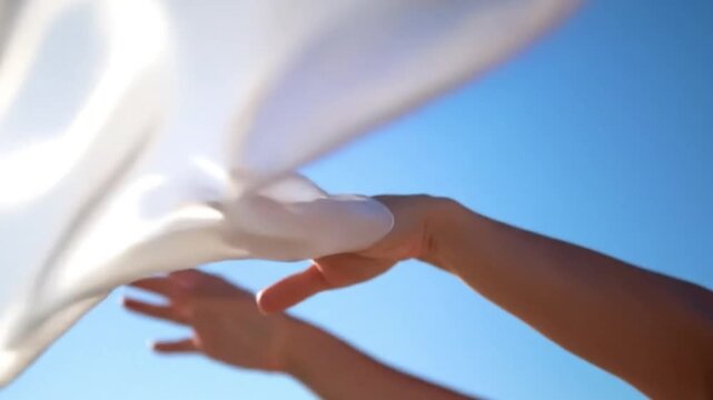 Hands waving white fabric against blue sky in bright sunlight  