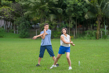 Obraz premium An Asian couple in athletic clothing walking together on a gravel path while holding hands, smiling and enjoying a peaceful moment in the countryside.