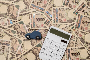 敷き詰められた多数の一万円札と電卓と自動車の模型