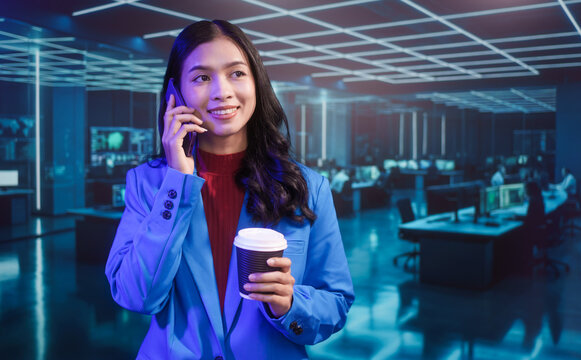 Smiling Asian professional woman in blue blazer uses mobile phone and holds coffee cup with futuristic IT room computer monitor office featuring neon lights and modern digital technology background. - Powered by Adobe