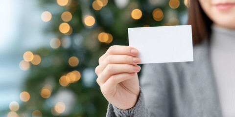 woman hand holding a blank business card mockup on a christmas tree background, with bokeh lights and shallow depth of field