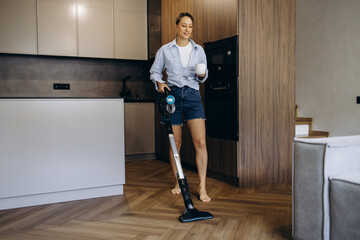 Woman vacuuming at home using rechargeable vacuum cleaner