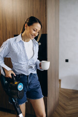 Woman vacuuming at home using rechargeable vacuum cleaner