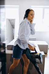 Woman vacuuming at home and listening to music in headphones