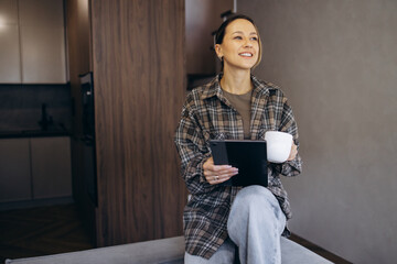 Woman working on tablet from home using tablet and drinking coffee