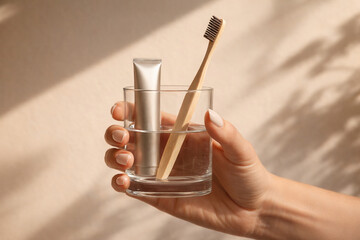 Eco friendly bamboo toothbrush and toothpaste in glass held by hand