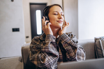 Woman using laptop and listening to music at home and sitting on sofa