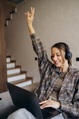 Woman using laptop and listening to music at home and sitting on sofa