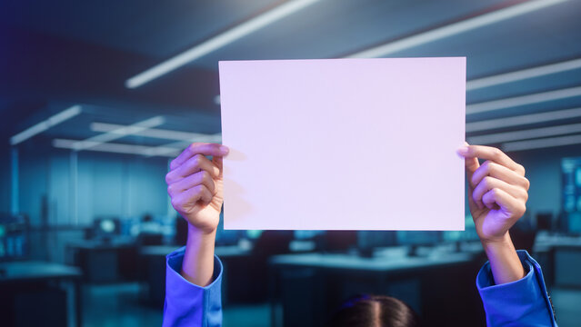 Smiling Asian woman holds blank white paper in high-tech office. This mockup template offers perfect copy space for business messages, advertisements, or announcements in futuristic setting.