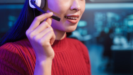 Friendly Asian customer support call center agent wears headset in high-tech control room. She provides professional online assistance and manages communications in busy digital operations center.