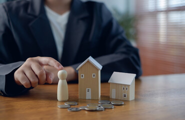Business person protecting wooden family figure and house models with coins on desk, concept of home insurance, financial security, mortgage planning, savings protection, wealth management.