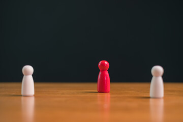Red wooden figure isolated between white figures on wooden table with dark background, minimal leadership and individuality concept showing separation, focus, decision making and authority.