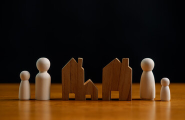 Wooden family figures and house shapes on wooden table with black background, minimal concept of family home, housing security, real estate planning, property ownership and life stability.