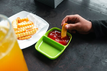 An enticing shot of a single french fry being dipped into ketchup, set beside a serving of crinkle cut fries and a refreshing beverage, all arranged on a dark table.