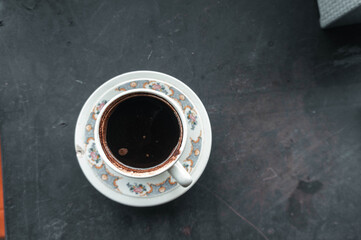 An inviting overhead shot captures a rich, dark coffee in a decorative cup, perched gracefully on its matching saucer. The still life evokes the aroma of a perfect moment of pause.