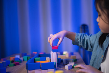 Cute Asian girl playing with wooden building blocks at night. Child learning and having fun with...