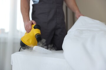Pest control worker cleaning bed with steam cleaner indoors, closeup