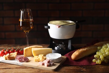 Fondue with tasty melted cheese, snacks and wine on wooden table