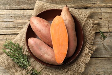 Raw sweet potatoes and rosemary on wooden table, top view