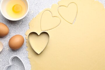 Obraz premium Raw dough, heart shaped cookie cutters, eggs and egg yolk in bowl on light gray textured table, flat lay
