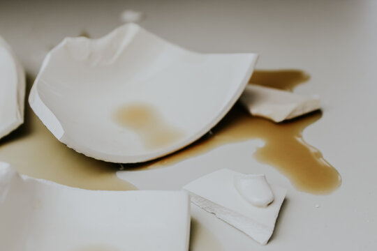 Close-up of a broken white ceramic cup and spilled coffee or tea. abstract background. metaphor for loss or irrevocable damage